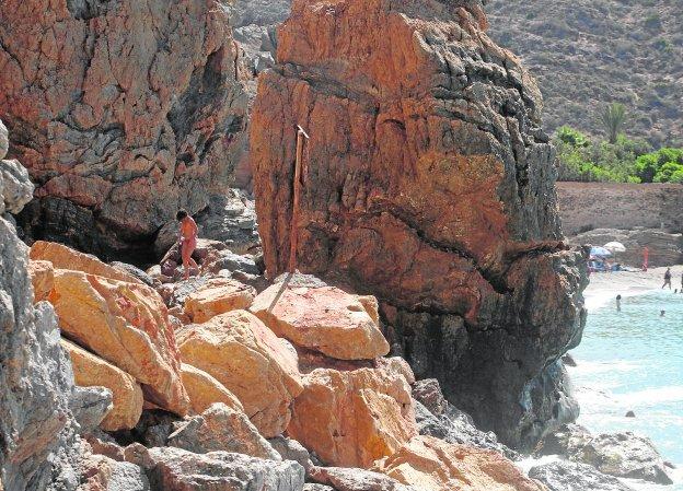 Un bañista baja a la playa de La Losa, en El Portús, por un grupo de rocas desprendidas del monte de Las Casillas.