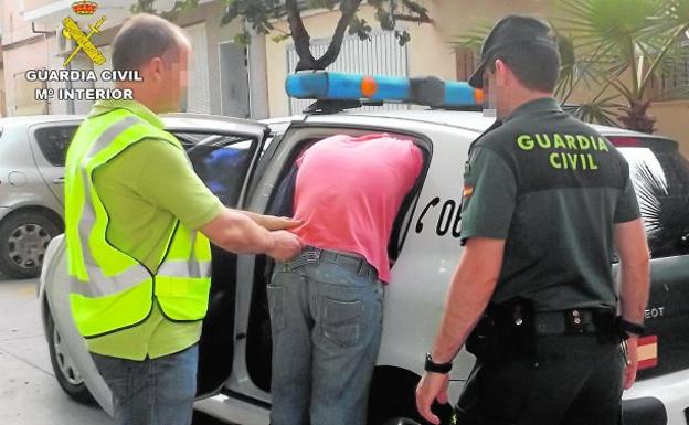 Dos agentes de la Guardia Civil introducen a uno de los detenidos en un coche patrulla.