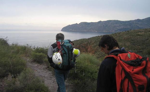 Dos excursionistas caminan con la silueta de Cabo Tiñoso a la vista.