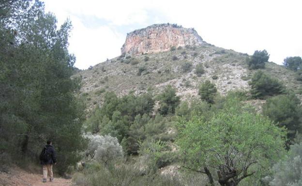 Un senderista camina por la falda de la montaña, con la Piedra del Castellar al fondo./