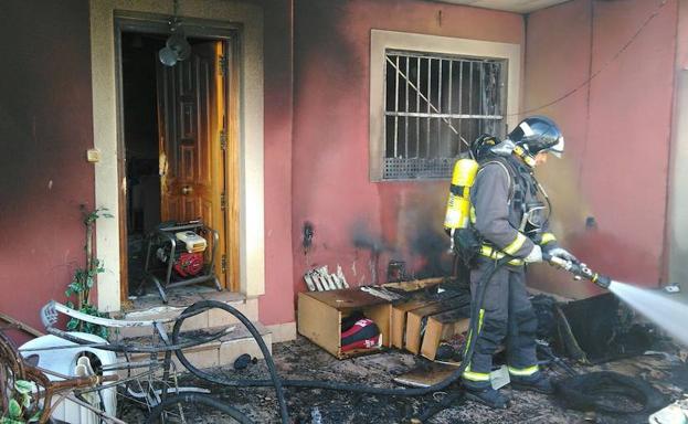 Un bombero sofoca las llamas en el porche de la vivienda incendiada. /112RM