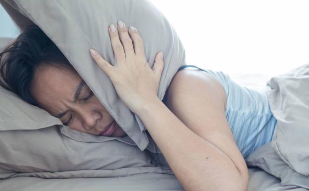 A woman covers herself with a cushion due to annoying snoring. 