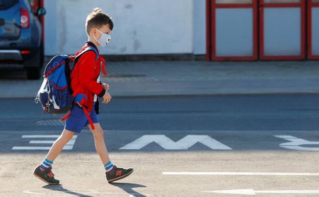 A boy heads to school carrying a backpack and wearing a mask. 