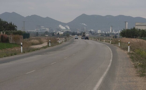 Cars and trucks cross a bumpy area on the La Aljorra highway, with the Sabic factory in the background. 