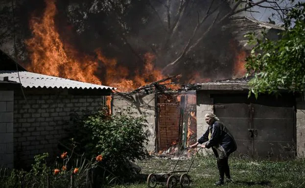 A woman walks with the remains of a cart past her burned-out house in Lisichans k, Donbas.