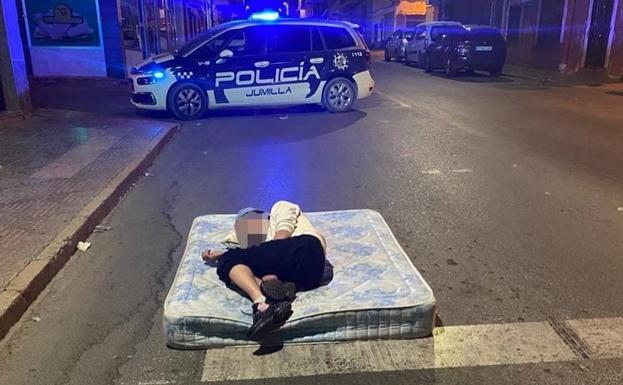 A man lying on a mattress in the middle of the road, on Yecla Avenue in Jumilla.