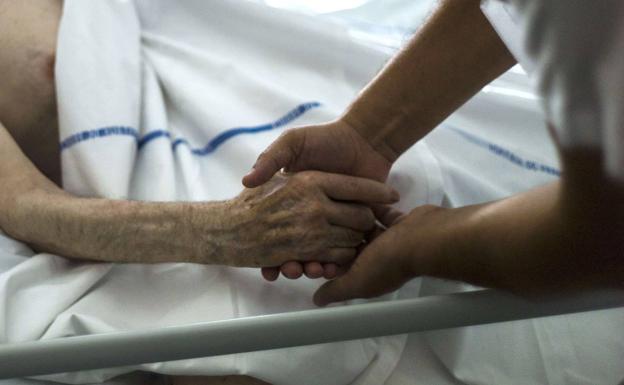 A health worker holds the hand of a terminally ill patient, in a file image. 