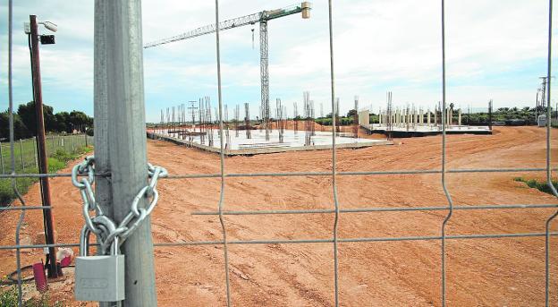 Entrance door to the construction works of the new La Aljorra school, with a padlock, and in the background the two modules that are being erected. 