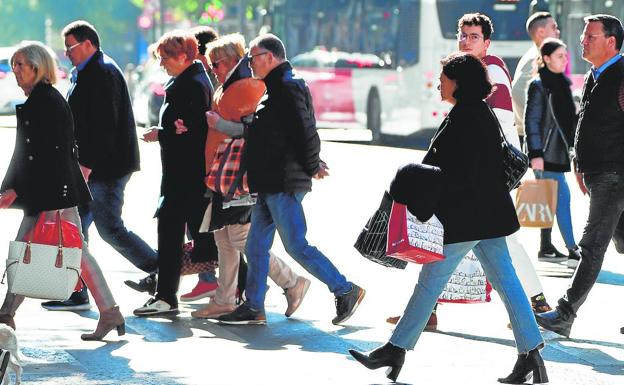 Several pedestrians loaded with bags walk along the Gran Vía in Murcia.